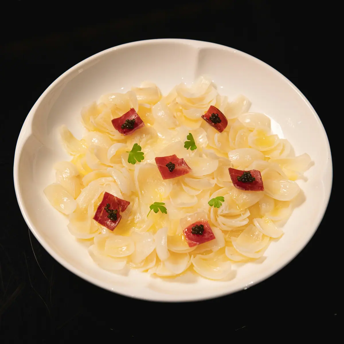 Лепестки кольраби с кусочками вяленого мяса и икрой на белой тарелке